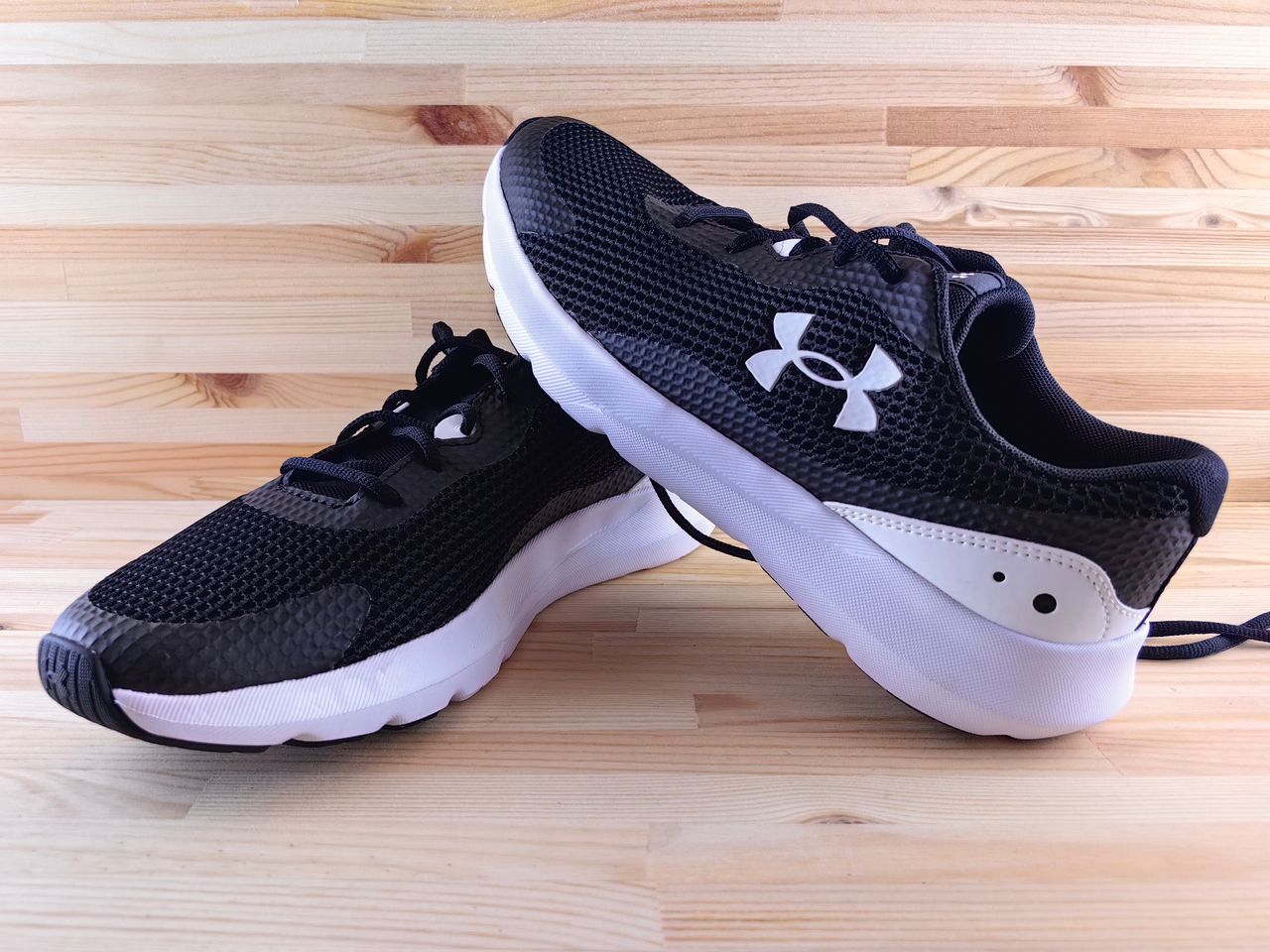 heros-img Stylish black athletic sneakers displayed on a wooden floor, perfect for sports and casual wear.